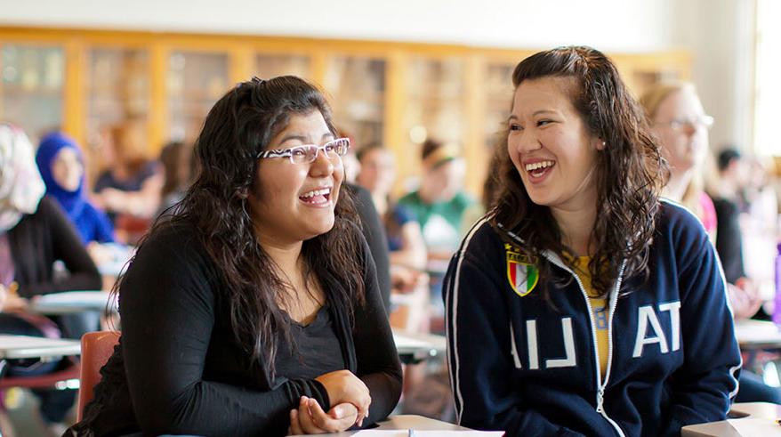 Two 学生 laughing in a classroom.